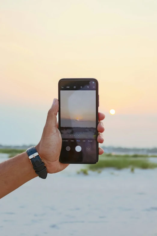 a hand holding up a phone in front of the ocean