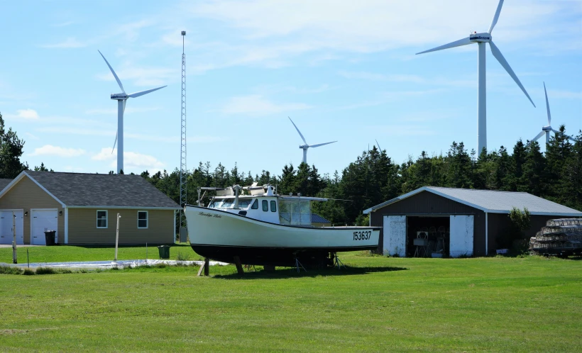 a small boat is on the grass in front of several wind turbines