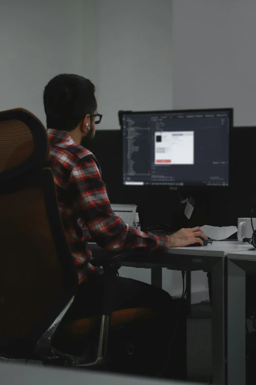 a man wearing glasses sitting at his desk looking at a computer screen