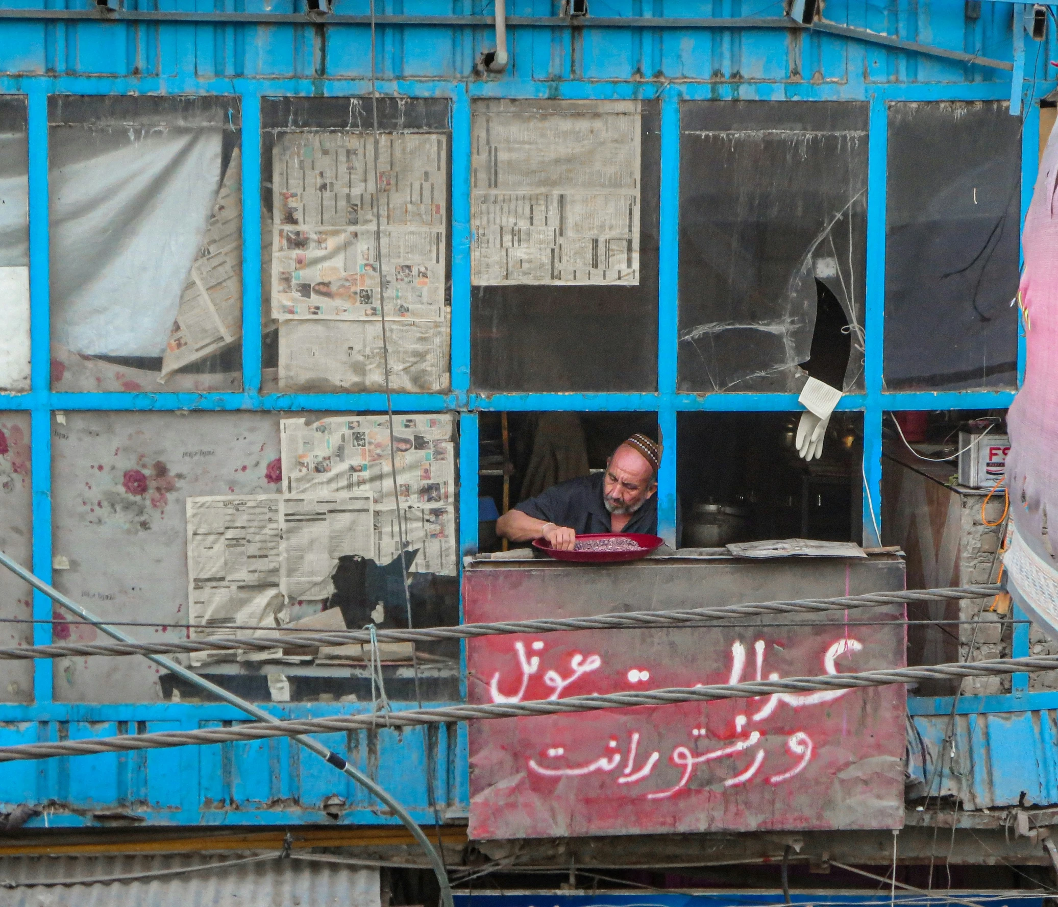 a man sits at his desk, in front of an old rusty building with posters in windows