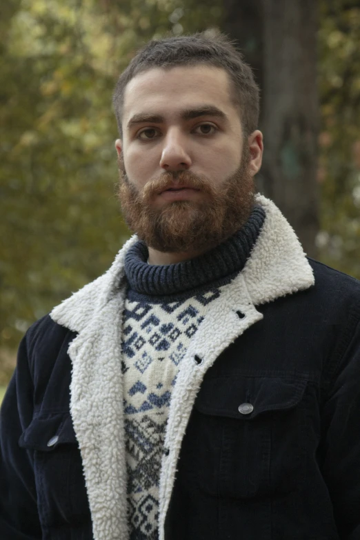 a man with a beard wearing a sweater looks into the camera