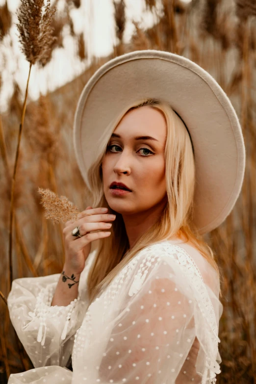 a beautiful blonde woman wearing a white hat in a field