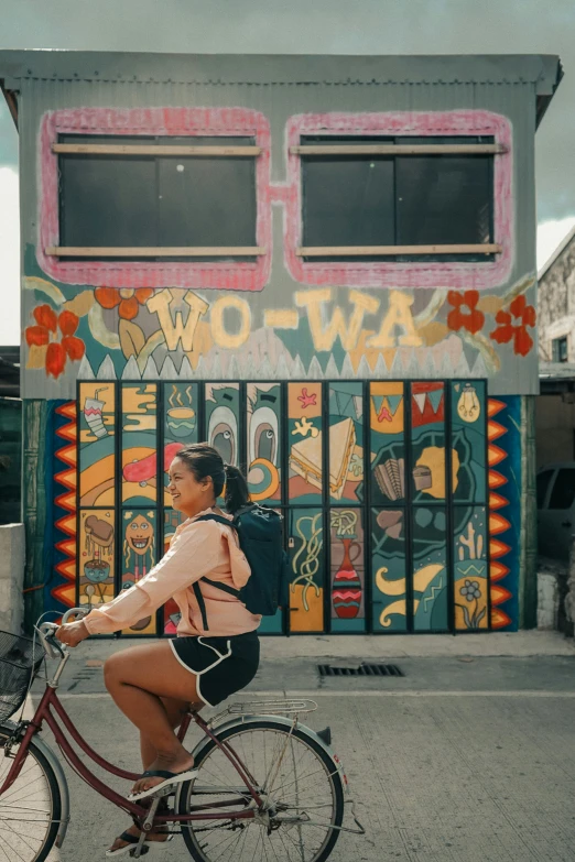 a girl in a sweater riding a bike by a wall painted with graffiti