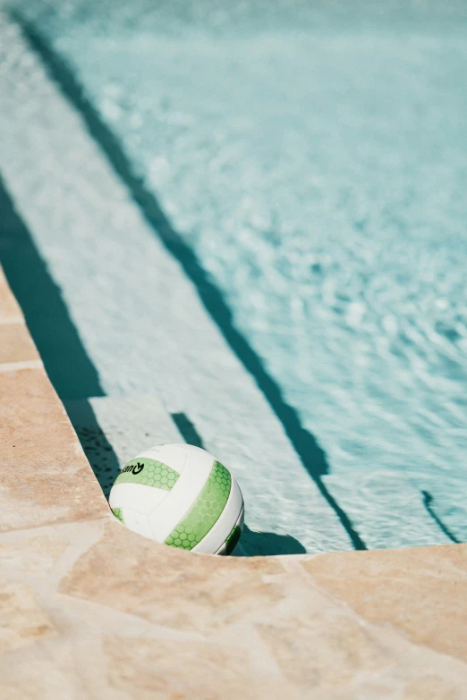 a volleyball ball laying in the ground by a pool