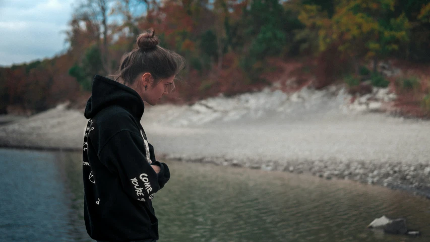 a man standing in front of a body of water wearing a hooded jacket