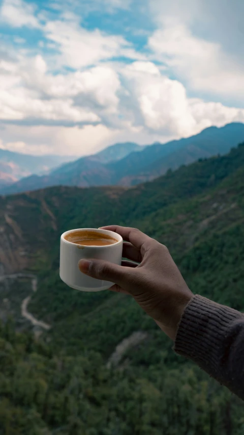 someone holds a cup of coffee up in front of the mountains