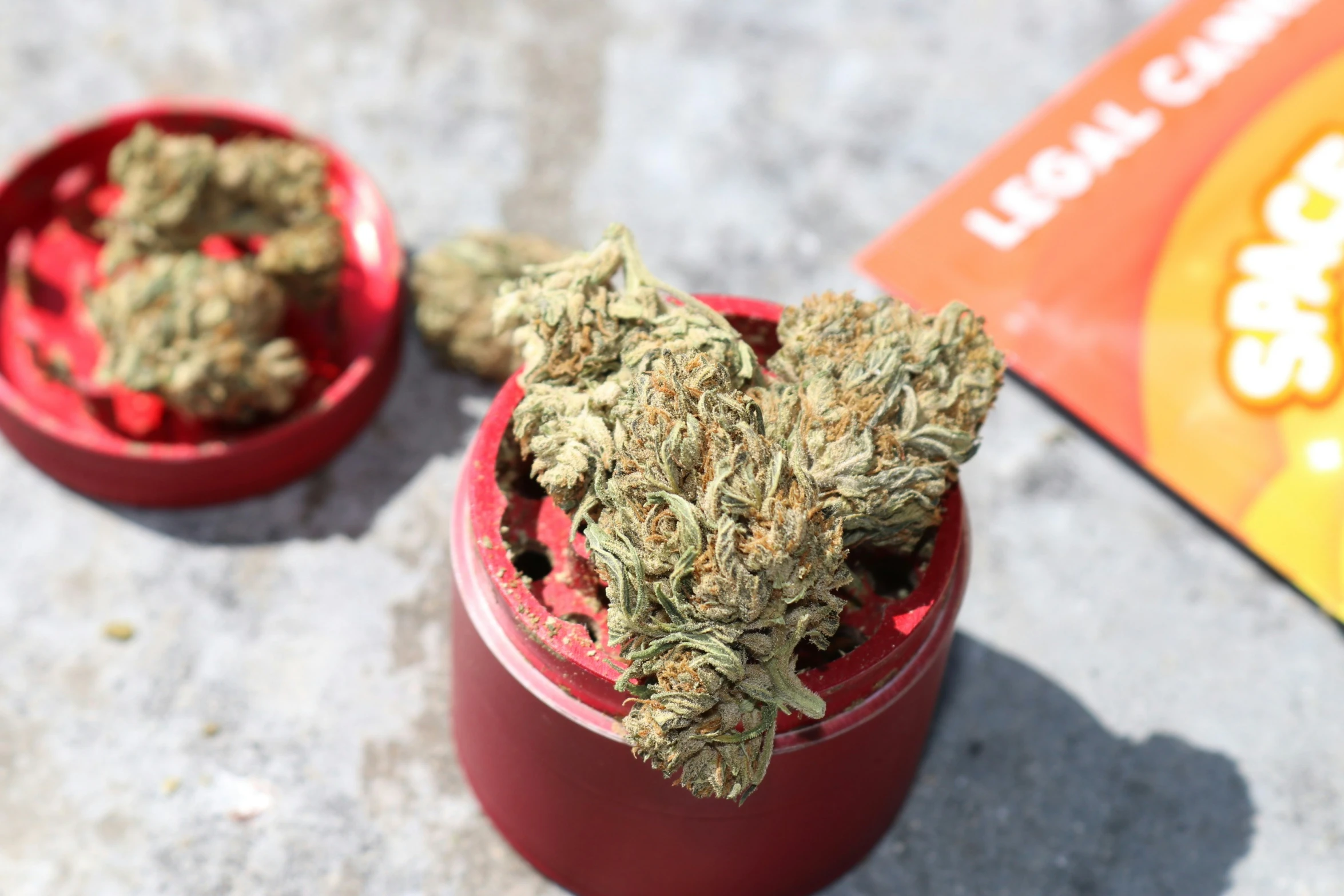 two red containers filled with weed next to an orange bag