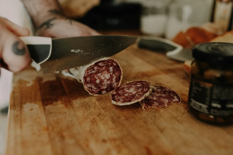 a man holding a knife  a piece of salami on a board