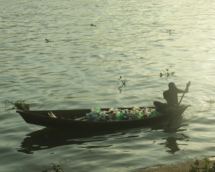 a man on a canoe with bags of garbage on the water