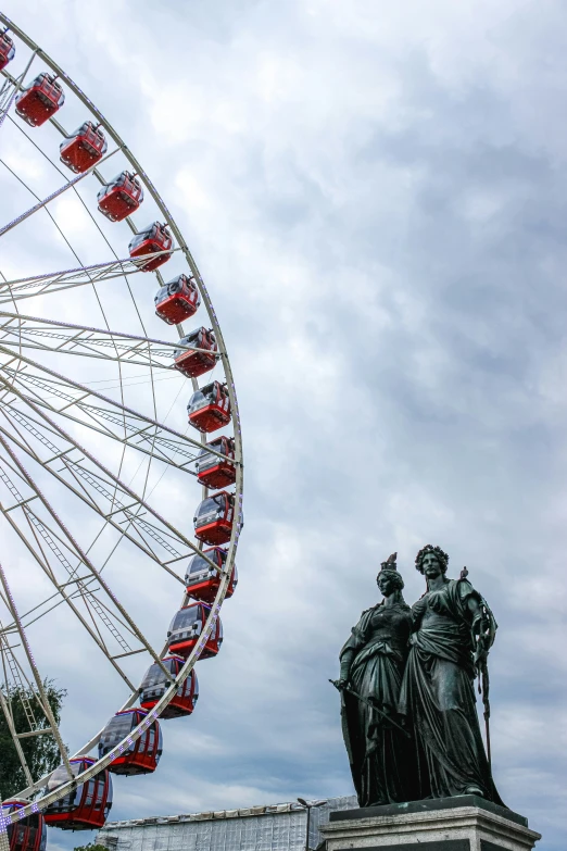 a statue and ferris wheel with cloudy skies in the background