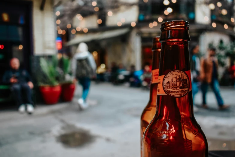 two beer bottles with people on the sidewalk behind them