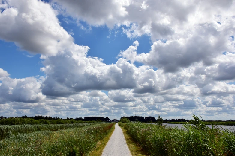 the dirt road leading to a lake under clouds