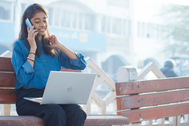 woman on bench using laptop while holding cellphone