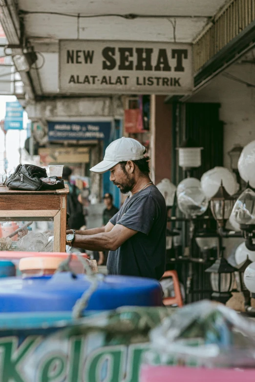 man in grey shirt and hat in front of market stand