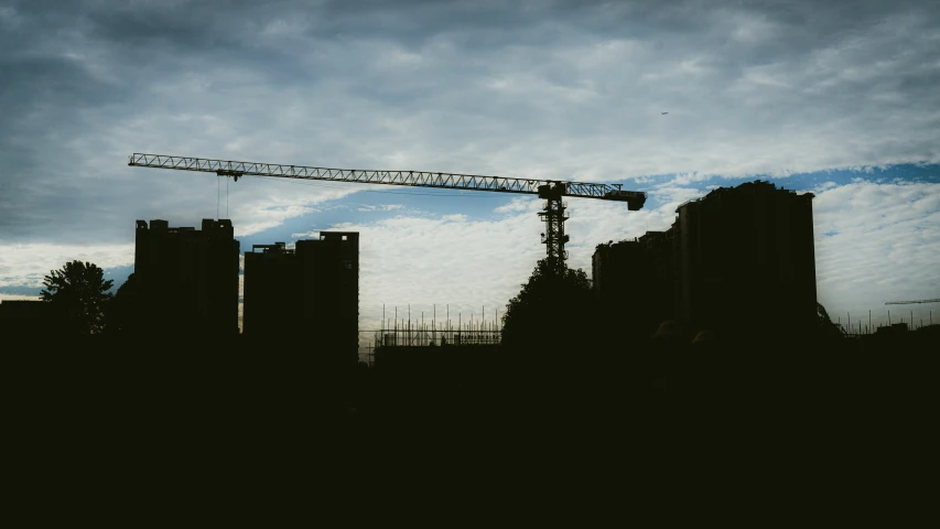 construction cranes are silhouetted against a cloudy sky