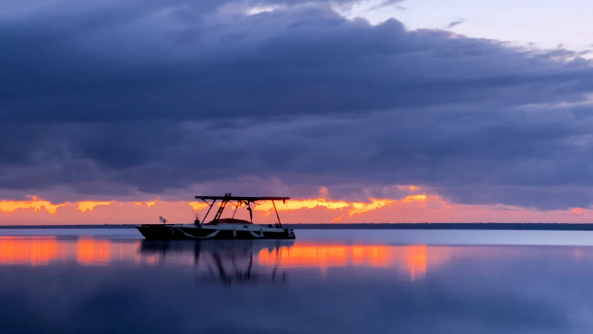 the sun sets in over a boat on the ocean