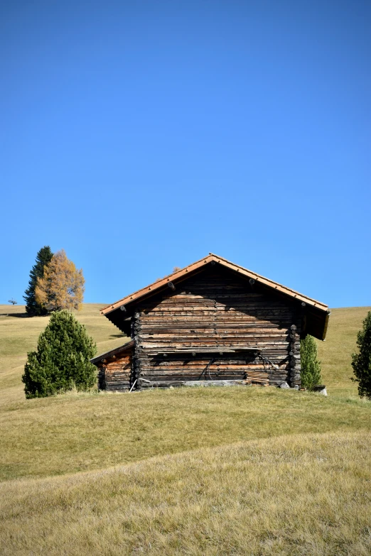 a small log cabin sits on the side of a grassy field