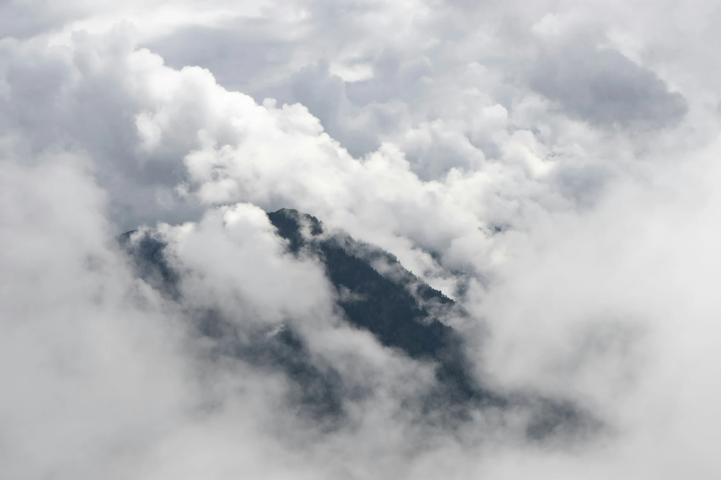 an airplane flying through the cloudy sky with mountains in the background