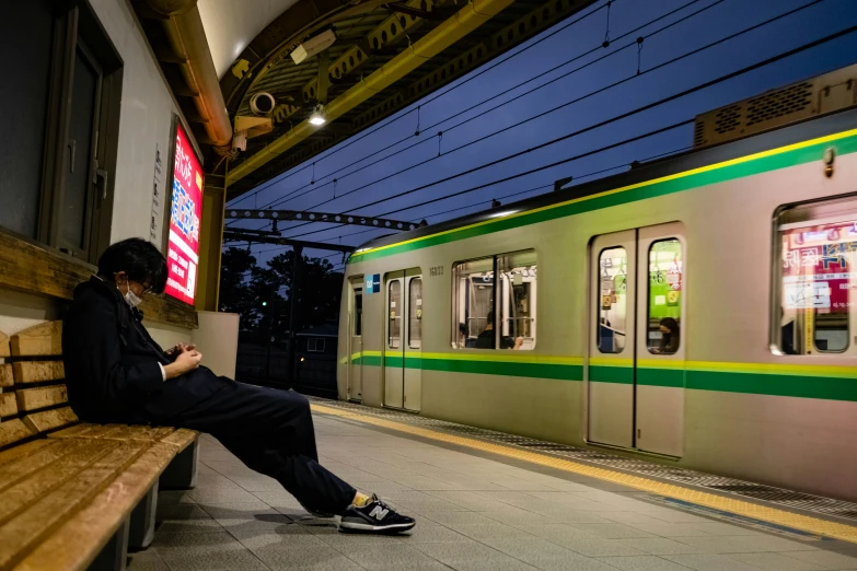 a man sitting on a bench at the platform with a train passing by