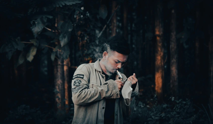 a man in jacket smoking soing by the woods