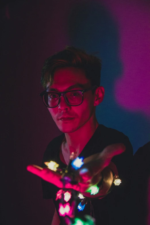 a man wearing glasses is pointing at a string light
