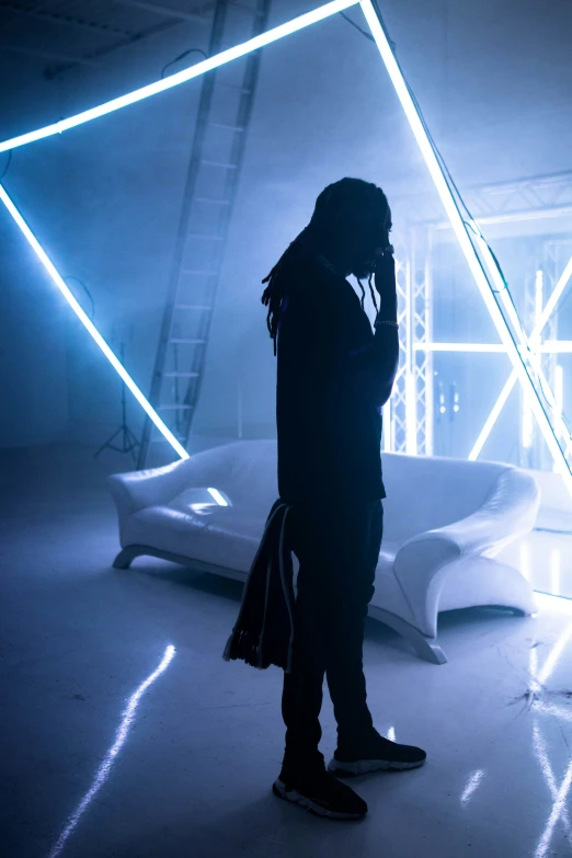 a man stands alone in a dark space in front of white furniture