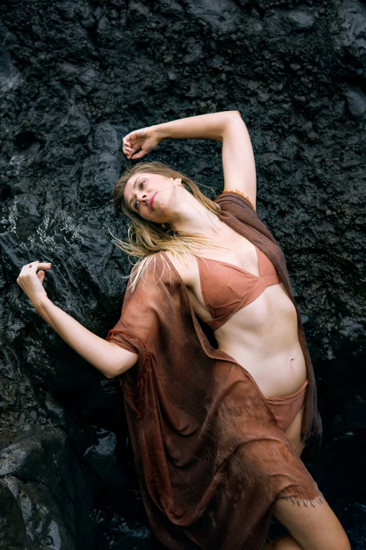 a beautiful woman in a brown dress lying on rocks