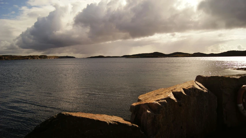 an island with a few hills in the background and clouds in the sky above it