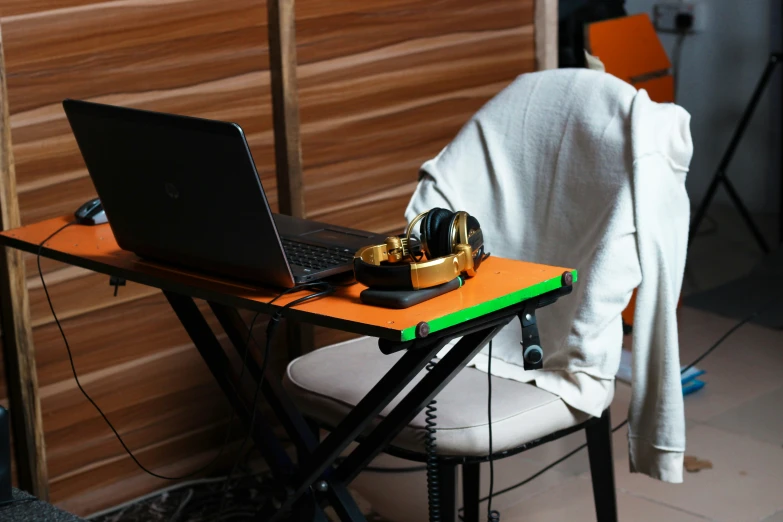 a laptop and headphones are resting on a wooden desk with a coat on top