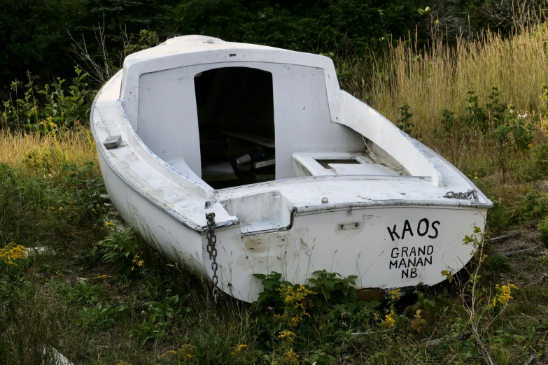 a boat sits abandoned in the grass by the woods