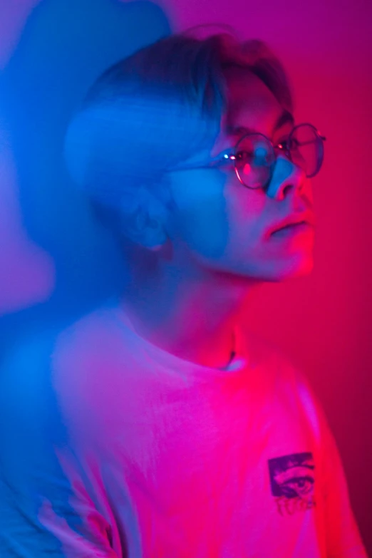 a young man in glasses posing with the camera in a pink and blue glow