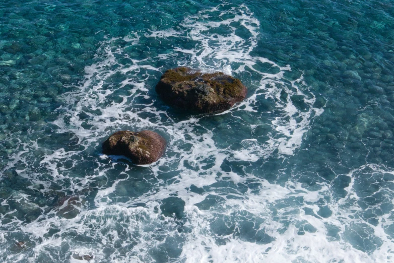 some rocks are in the water by the shore