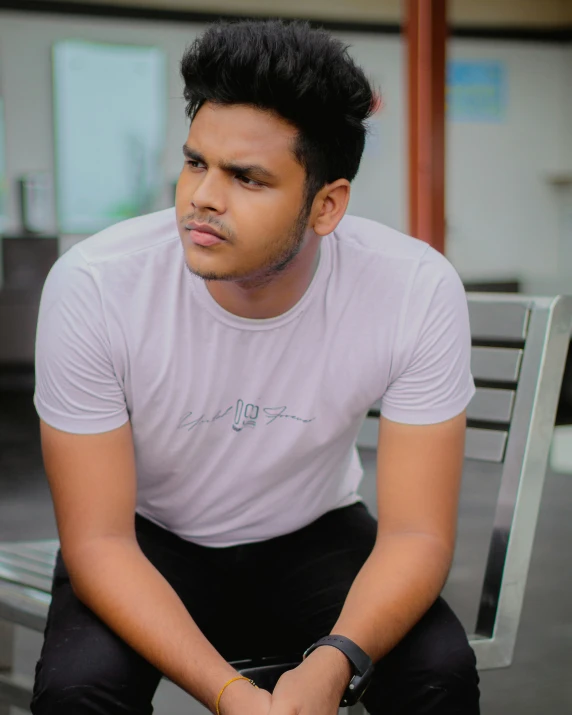 a guy with his hand in his pocket while sitting on a bench