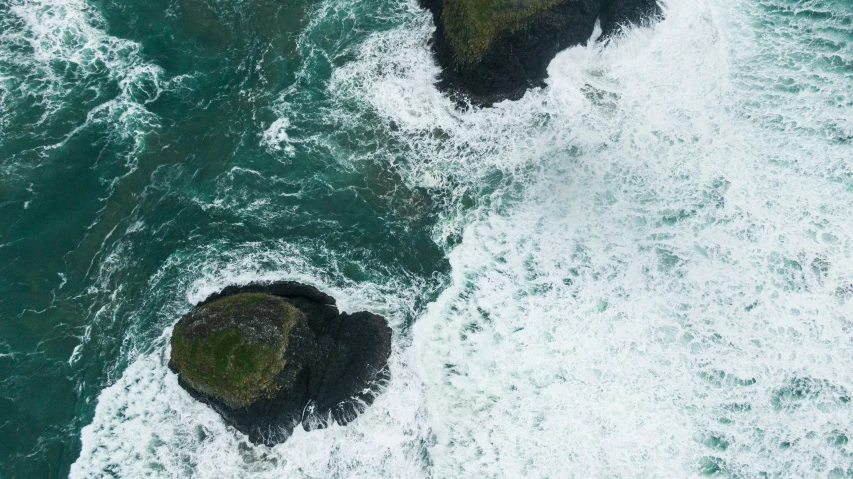 two rocky outcrops sitting on top of the ocean next to an island