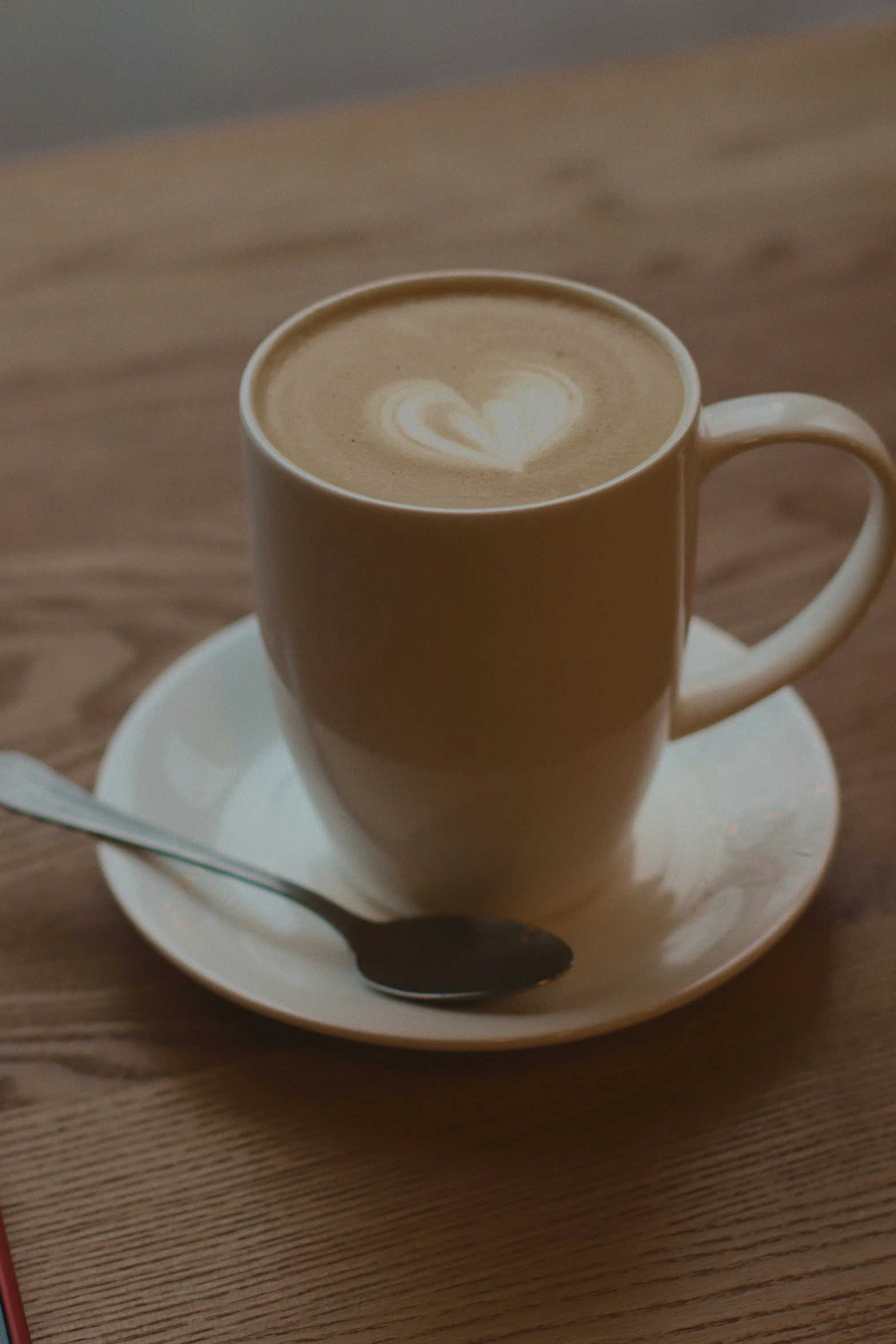 a plate holding a spoon, bowl and coffee cup on a wooden surface