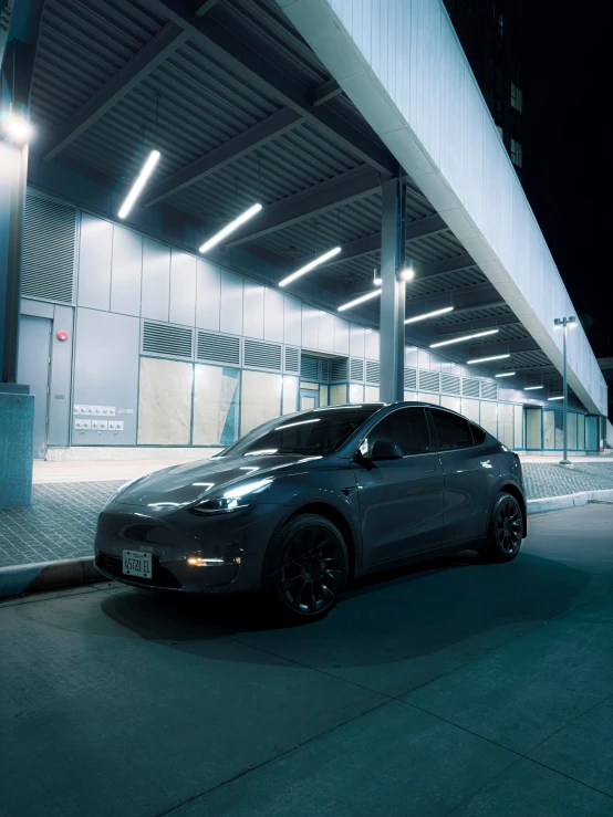 the large, sleek electric car sits parked under a bridge