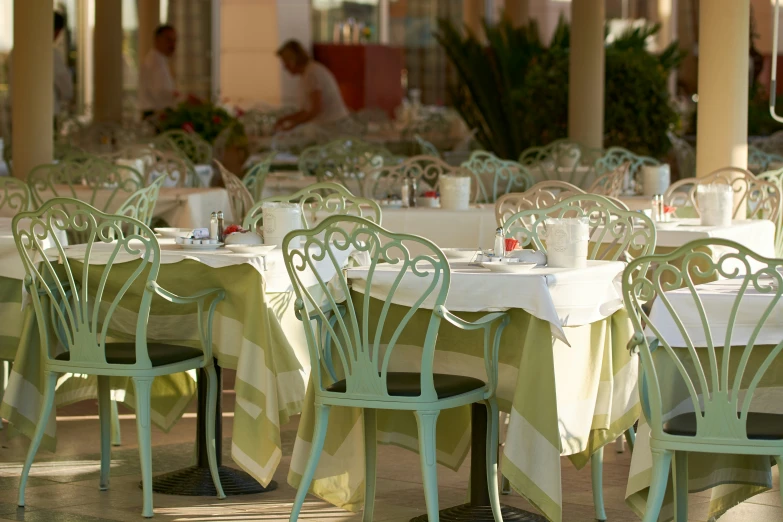 many chairs are around table with white and green cloth
