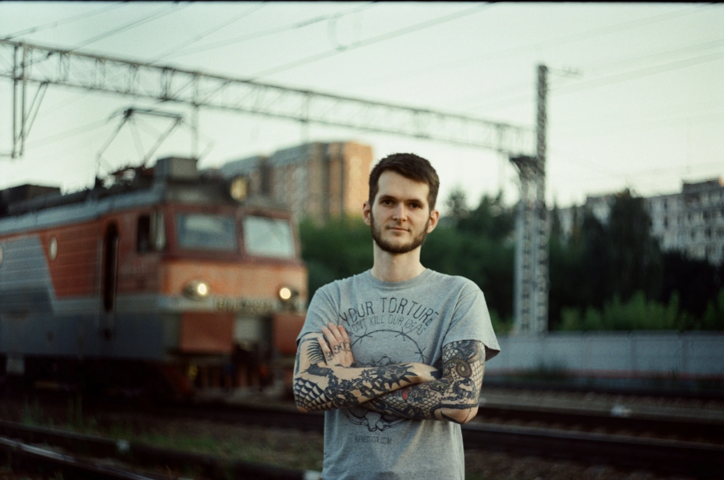 a man with tattoos stands next to a train on the tracks