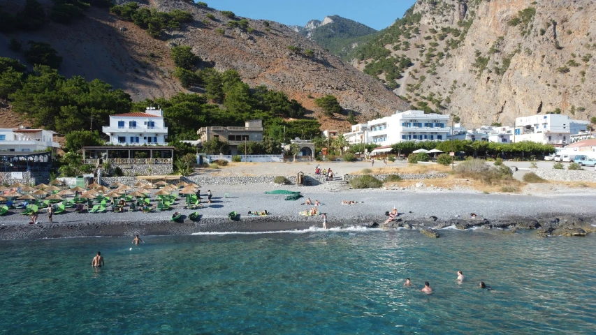 people are swimming at the beach near mountains