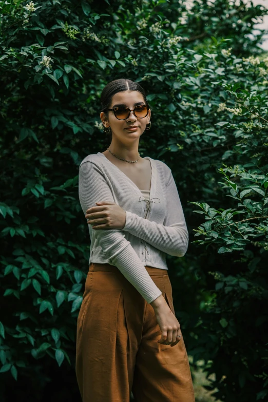 a woman standing in front of a bush, wearing a sweater