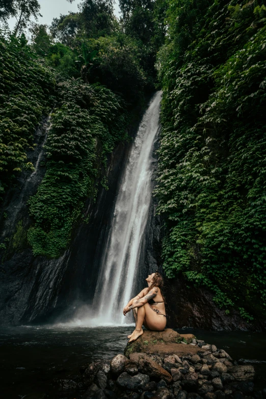 a person sitting on a rock near a waterfall