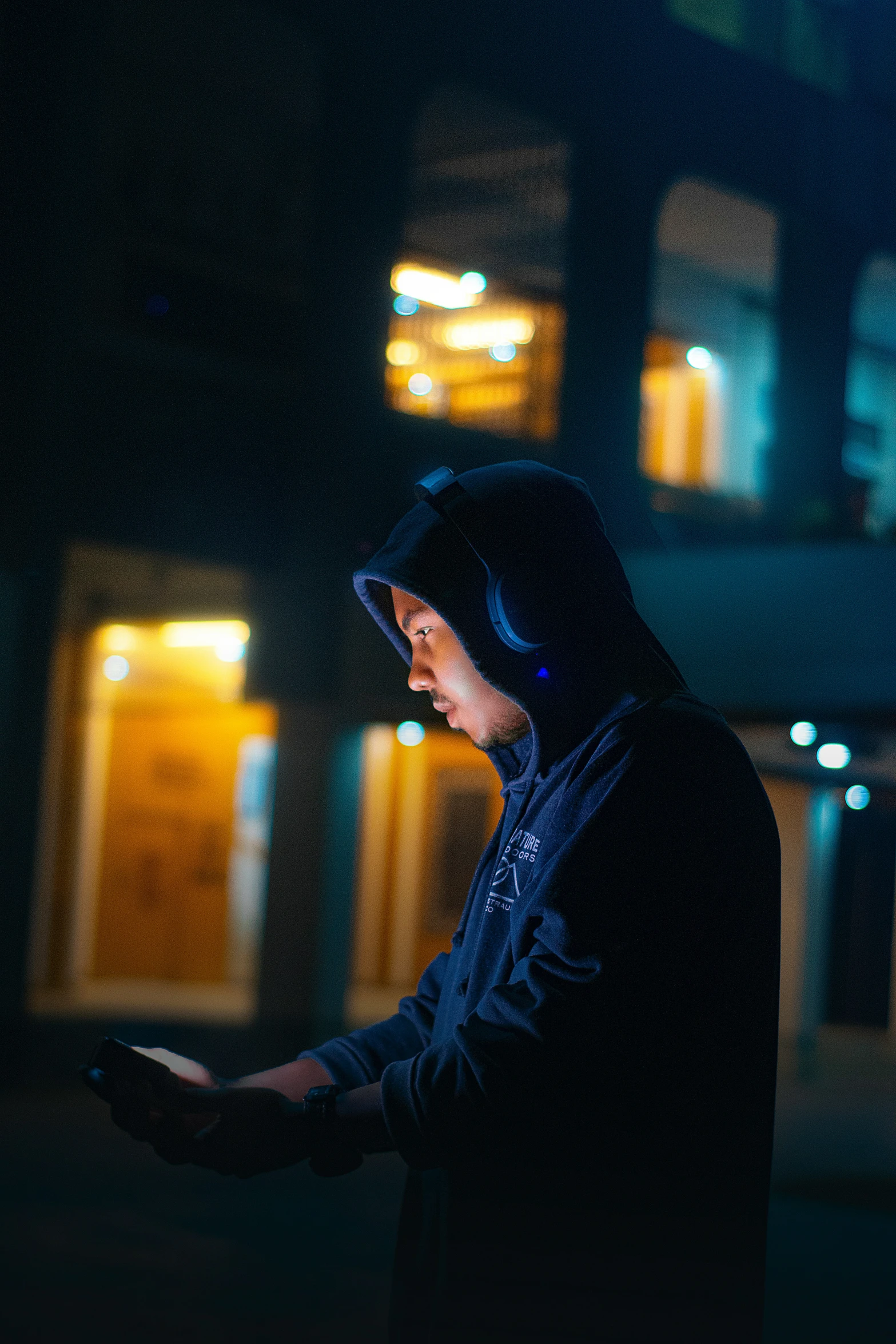 person in hoodie using cellphone in front of a building at night