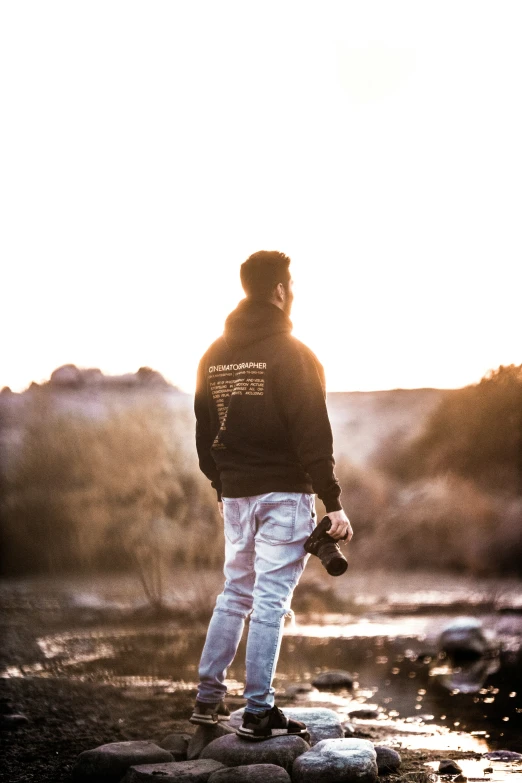 a man stands on rocks at the edge of a river