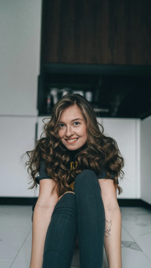 a woman with long hair smiling while sitting on the floor