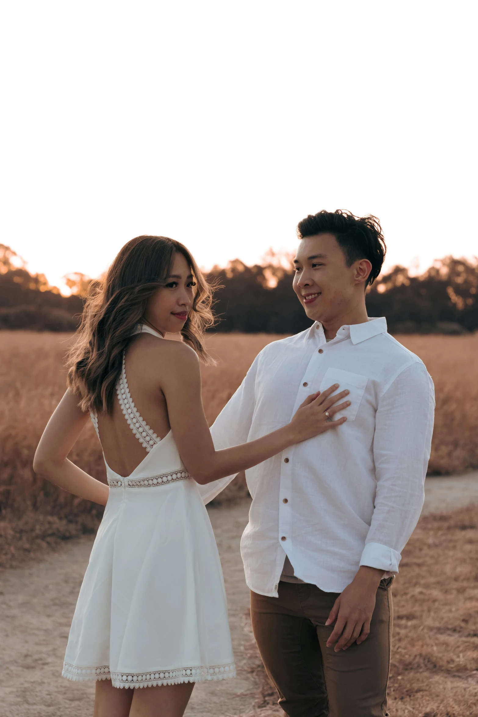 a couple poses in front of some tall grass at sunset