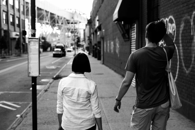 two young people walk down the sidewalk while one holds onto his hand