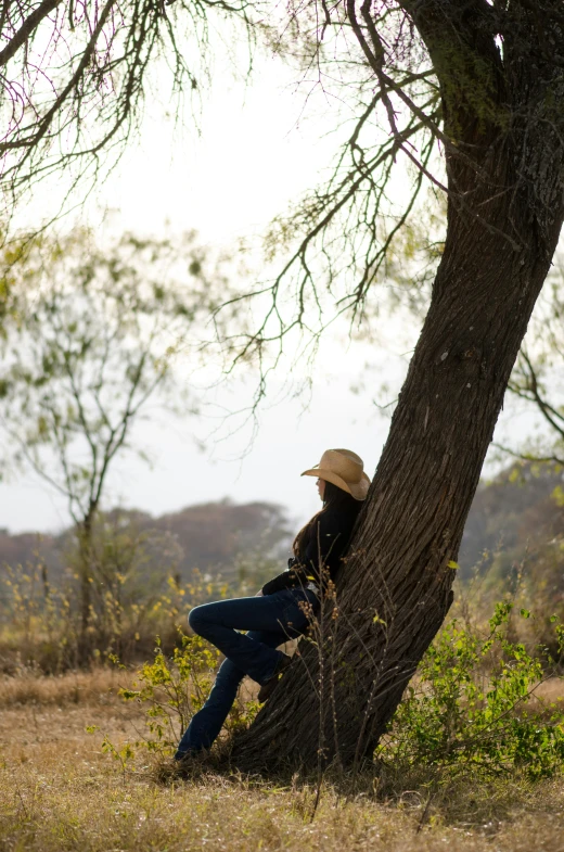 the woman is sitting against the tree while she looks back