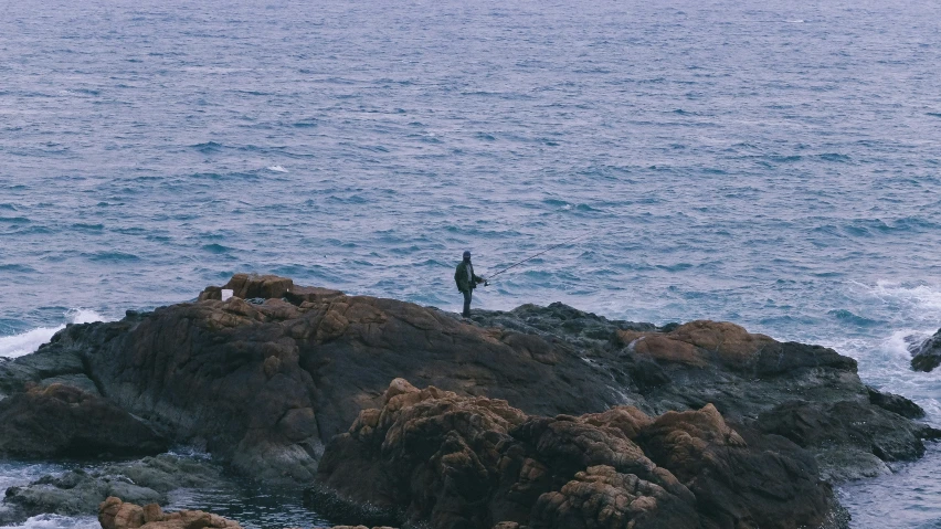 a man fishing from the side of a rock in the ocean