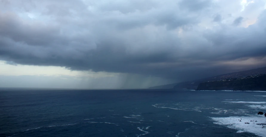 large storm clouds hover over the ocean, overlooking the shore