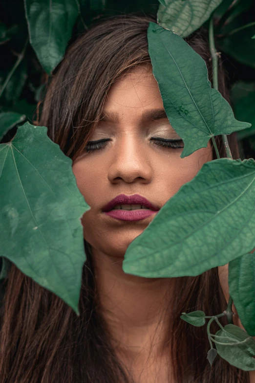 a woman with leaves covering her face next to plants